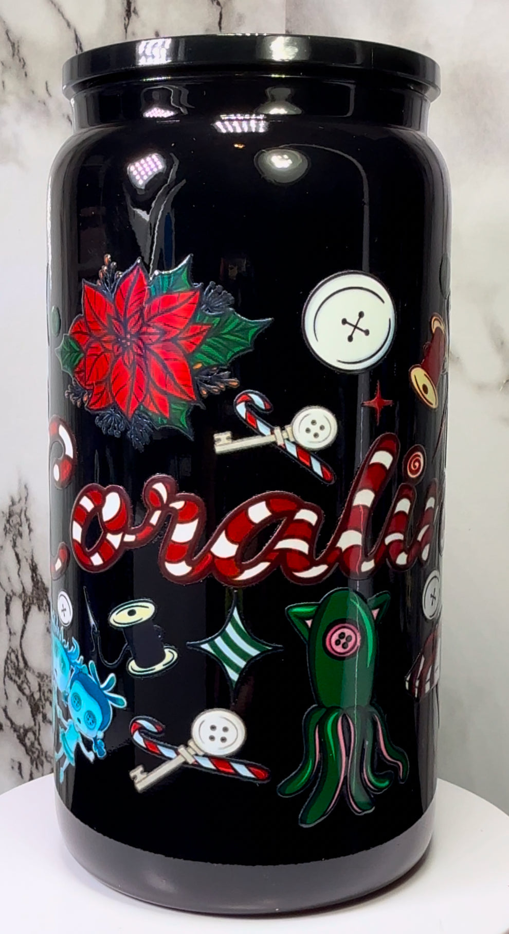 Coraline Christmas UVDTF on either a black plastic or black glass beer can cup